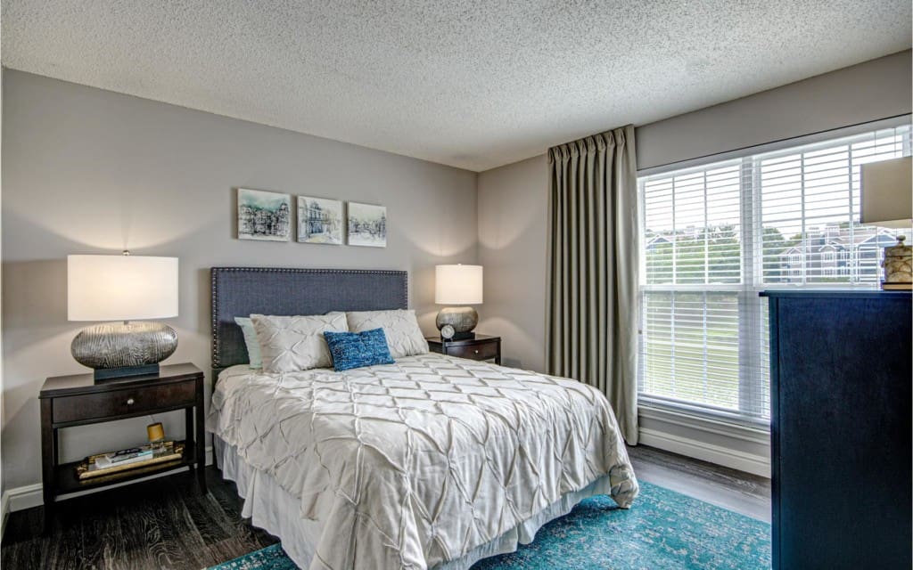 Two BR Apartments in Centreville, VA - Lakeside - Bedroom with Bed, Nightstands with Lamps, Dresser, Area Rug, and Large Window with Curtains.